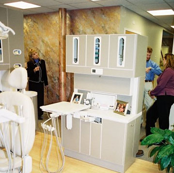 Showroom display of white cabinetry and dental equipment with backdrop and plants.