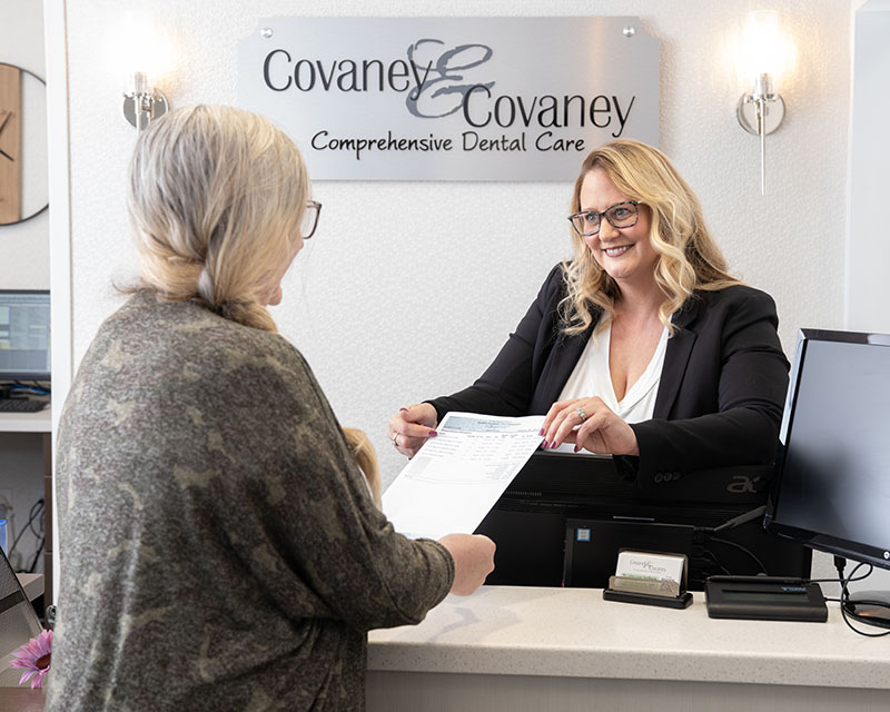Receptionist assisting patient at Covaney & Covaney dental office front desk.