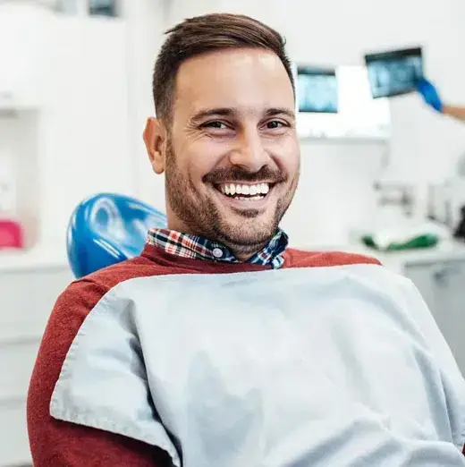 Smiling man wearing red cape in dental office setting with equipment visible.
